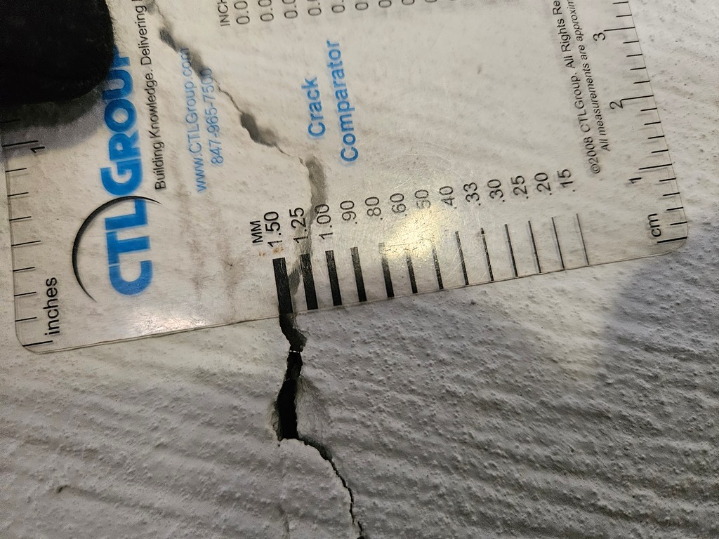 Using a crack width gauge to measure the size of a crack on a basement foundation wall