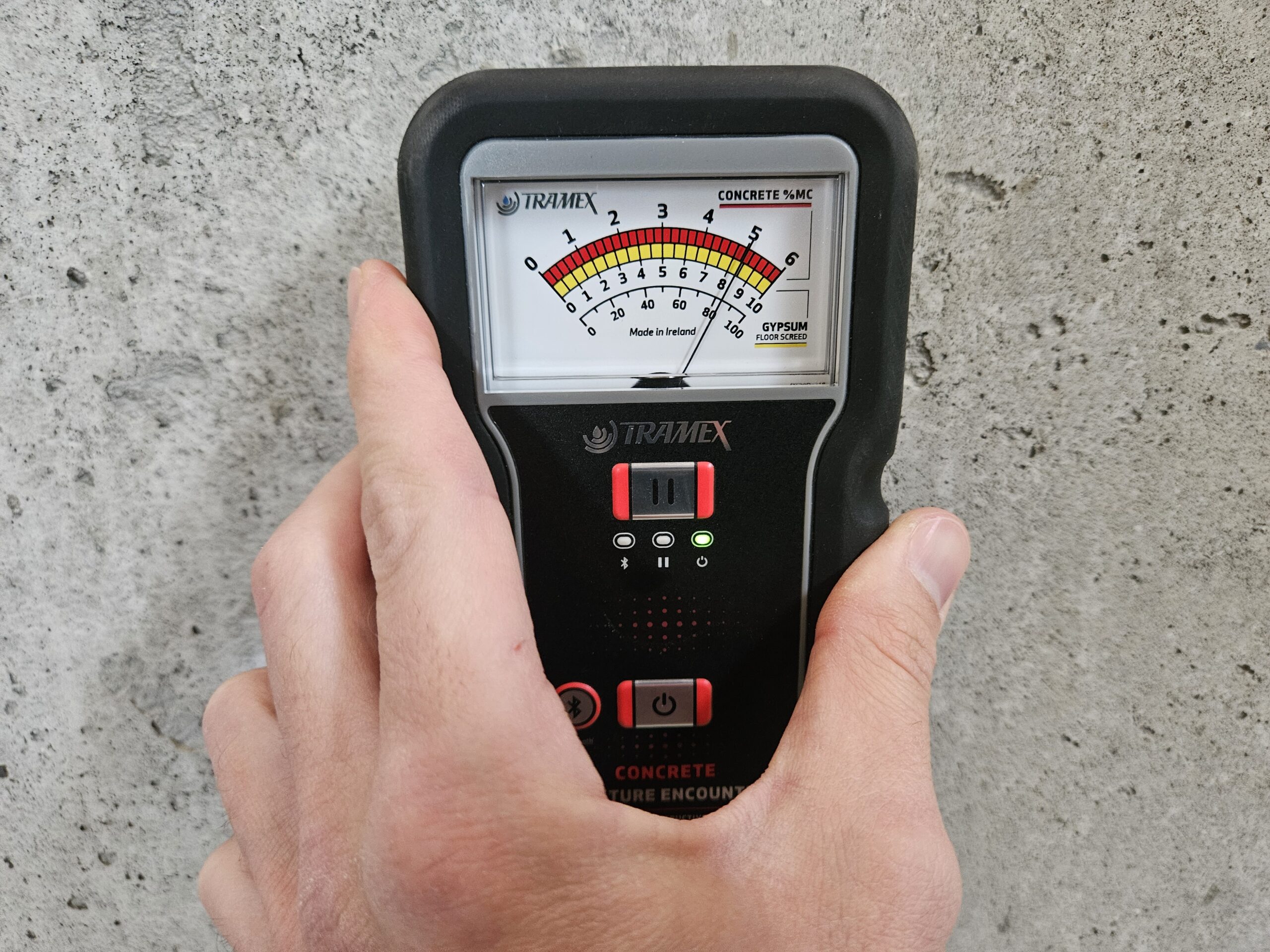 Moisture meter placed on a concrete basement wall to measure moisture content in the substrate