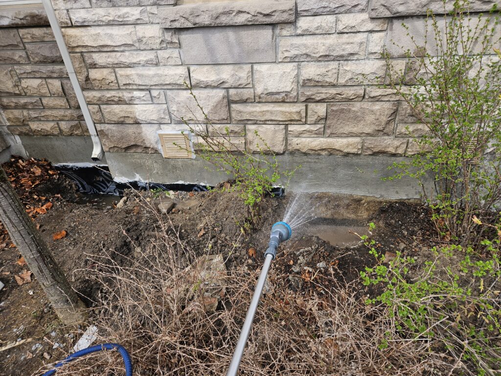 Spraying the exterior foundation wall with a garden hose set to shower mode during a basement leak test
