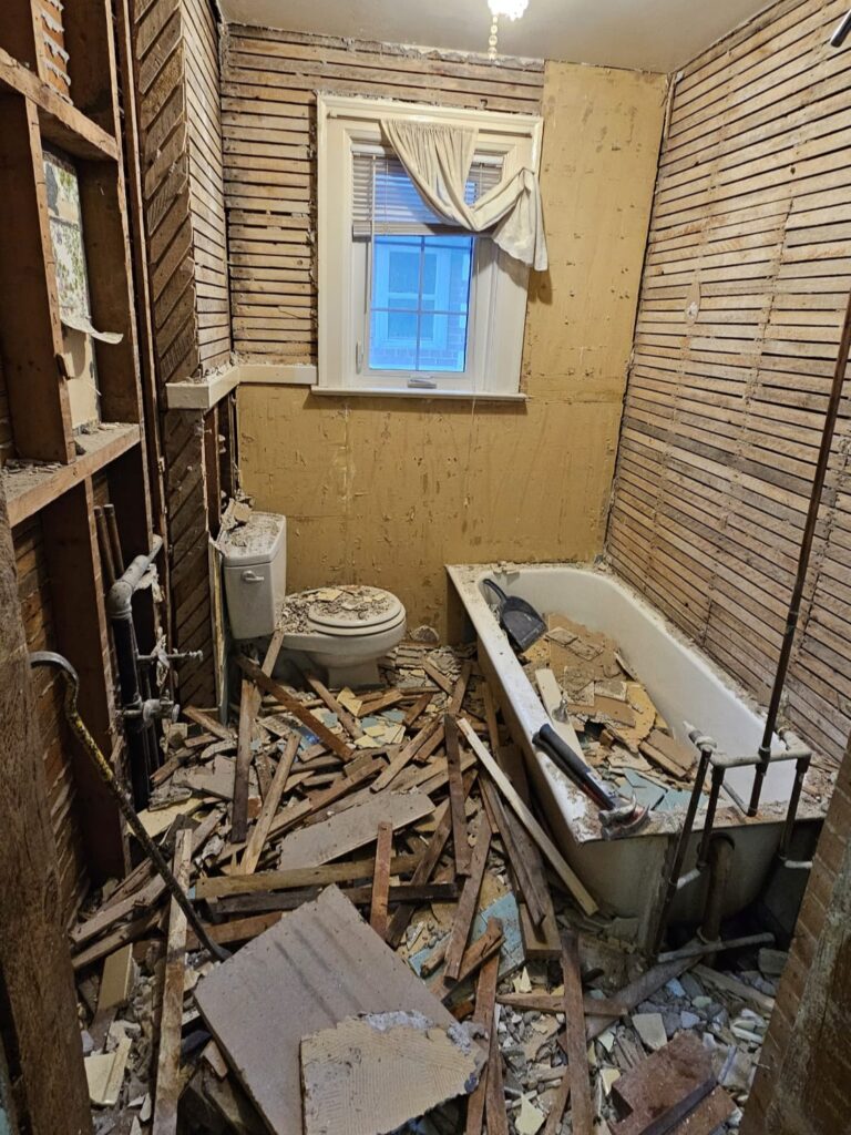 Bathroom demolition in Midtown Toronto with walls stripped to studs and debris on floor, showing full layout change by Olive Contractors