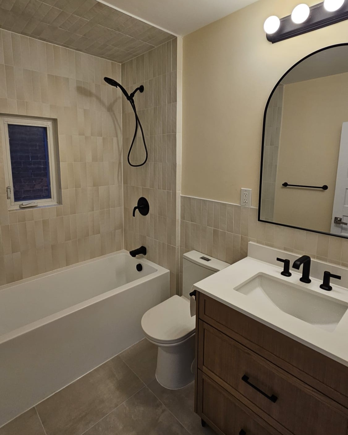 Fully finished modern bathroom renovation with freestanding tub, large format tiles, wood vanity, black fixtures, and in-floor heating system
