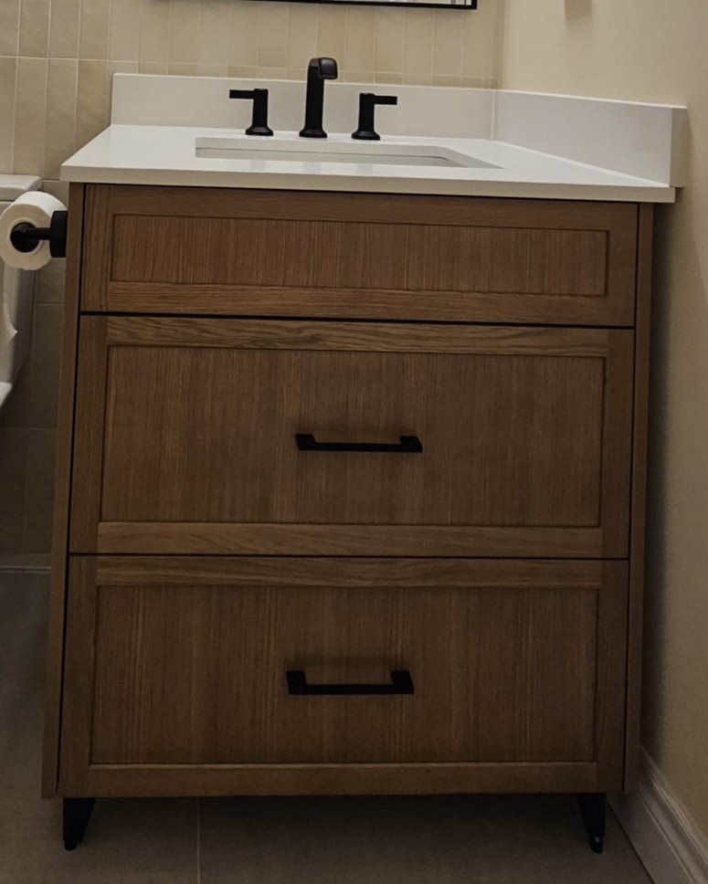 Bathroom vanity featuring warm wood cabinetry, matte black hardware, and a quartz sink in a modern bathroom renovation.