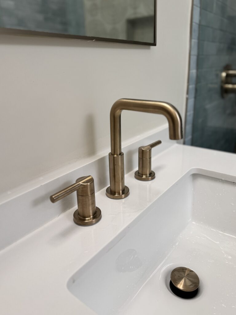 Close-up of brushed brass widespread faucet on white quartz countertop in renovated ensuite bathroom Toronto