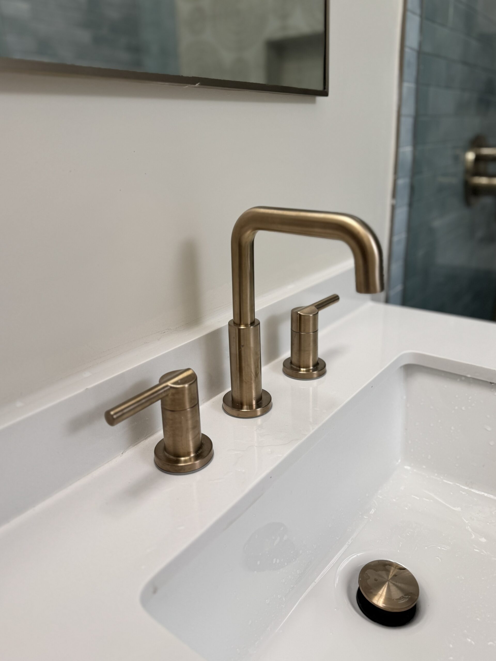 Close-up of brushed brass widespread faucet on white quartz countertop in renovated ensuite bathroom Toronto