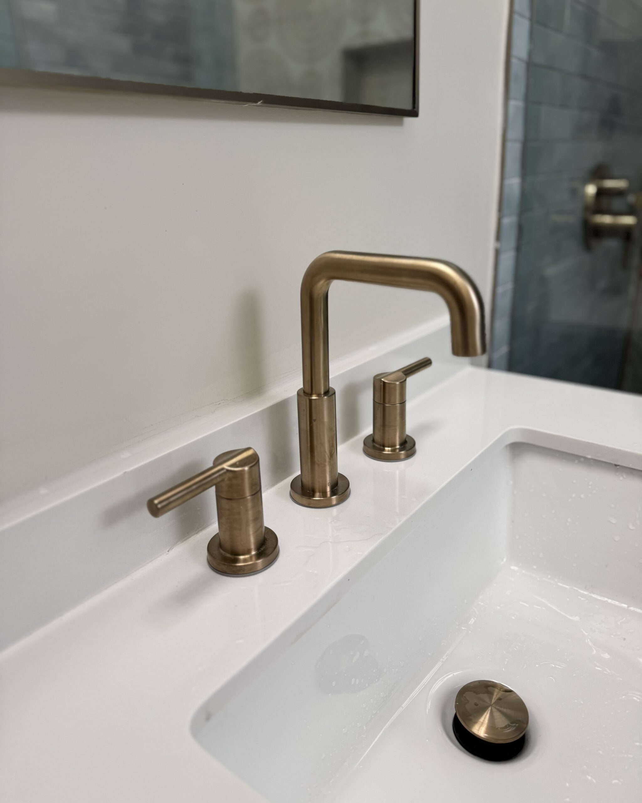 Close-up of brushed brass widespread faucet on white quartz countertop in renovated ensuite bathroom Toronto