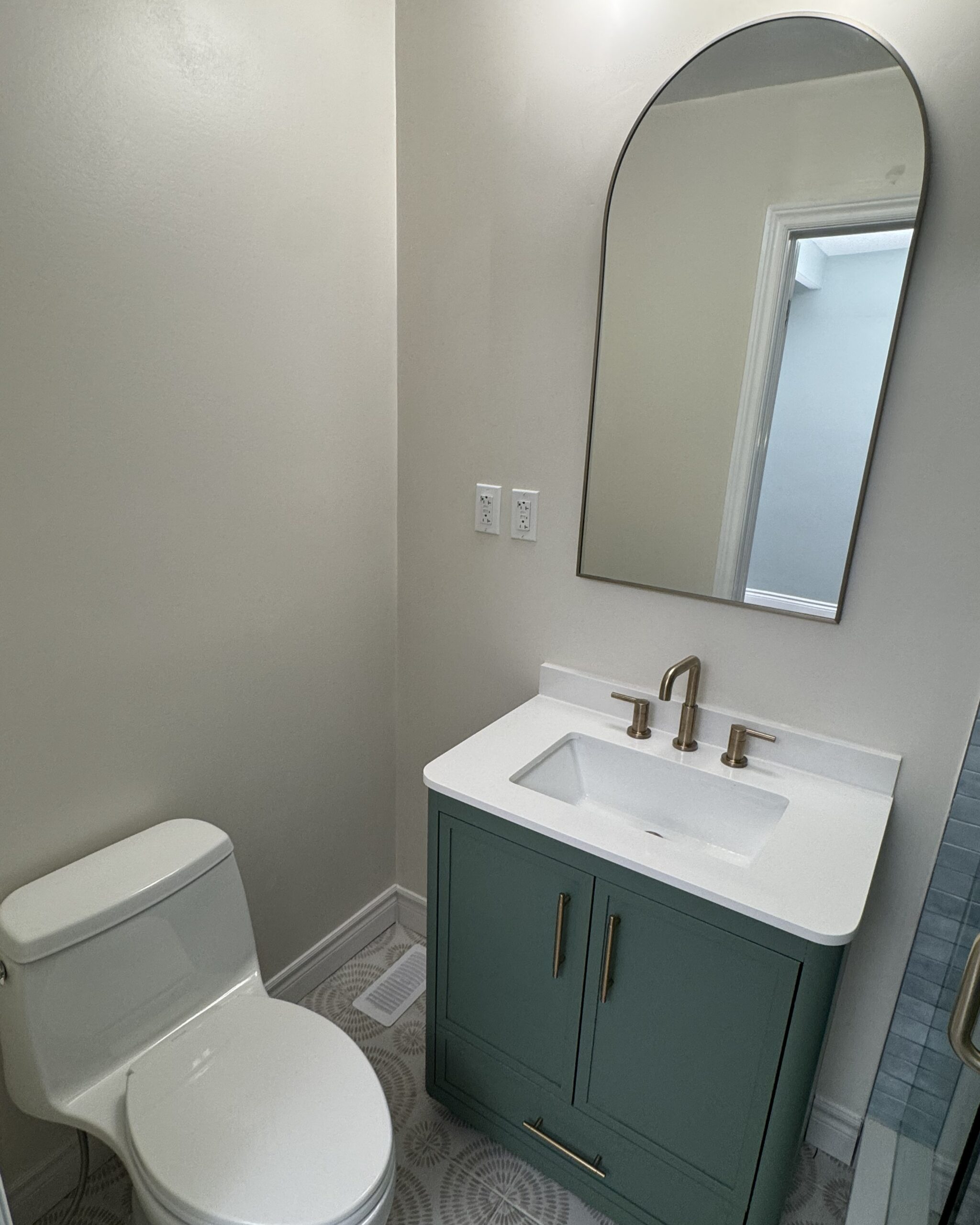 Renovated ensuite bathroom with forest green vanity, white quartz countertop, arched mirror, and brushed brass faucet in Toronto