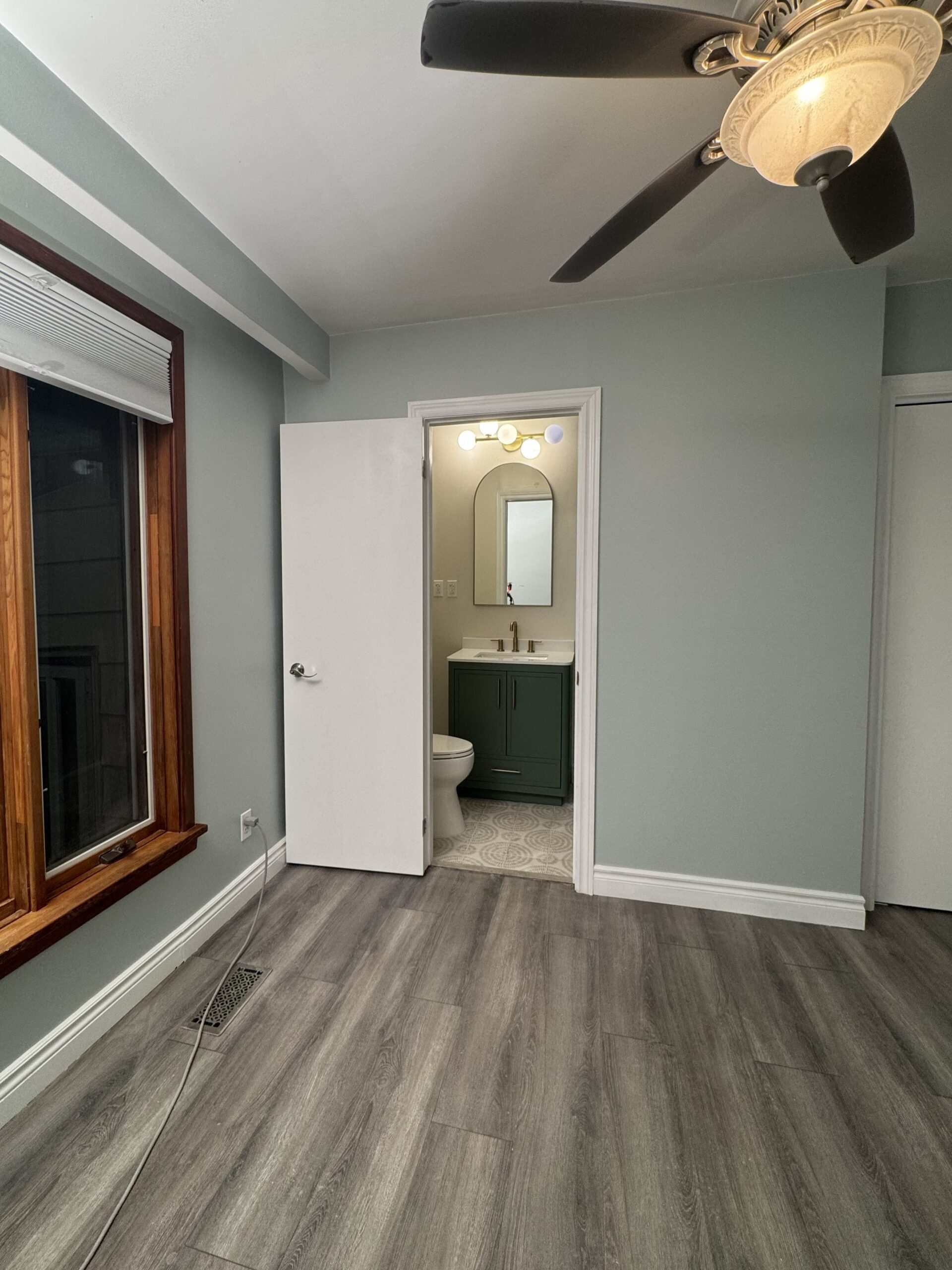 Renovated master bedroom with new grey LVP flooring and open doorway leading to newly added ensuite bathroom in Toronto home