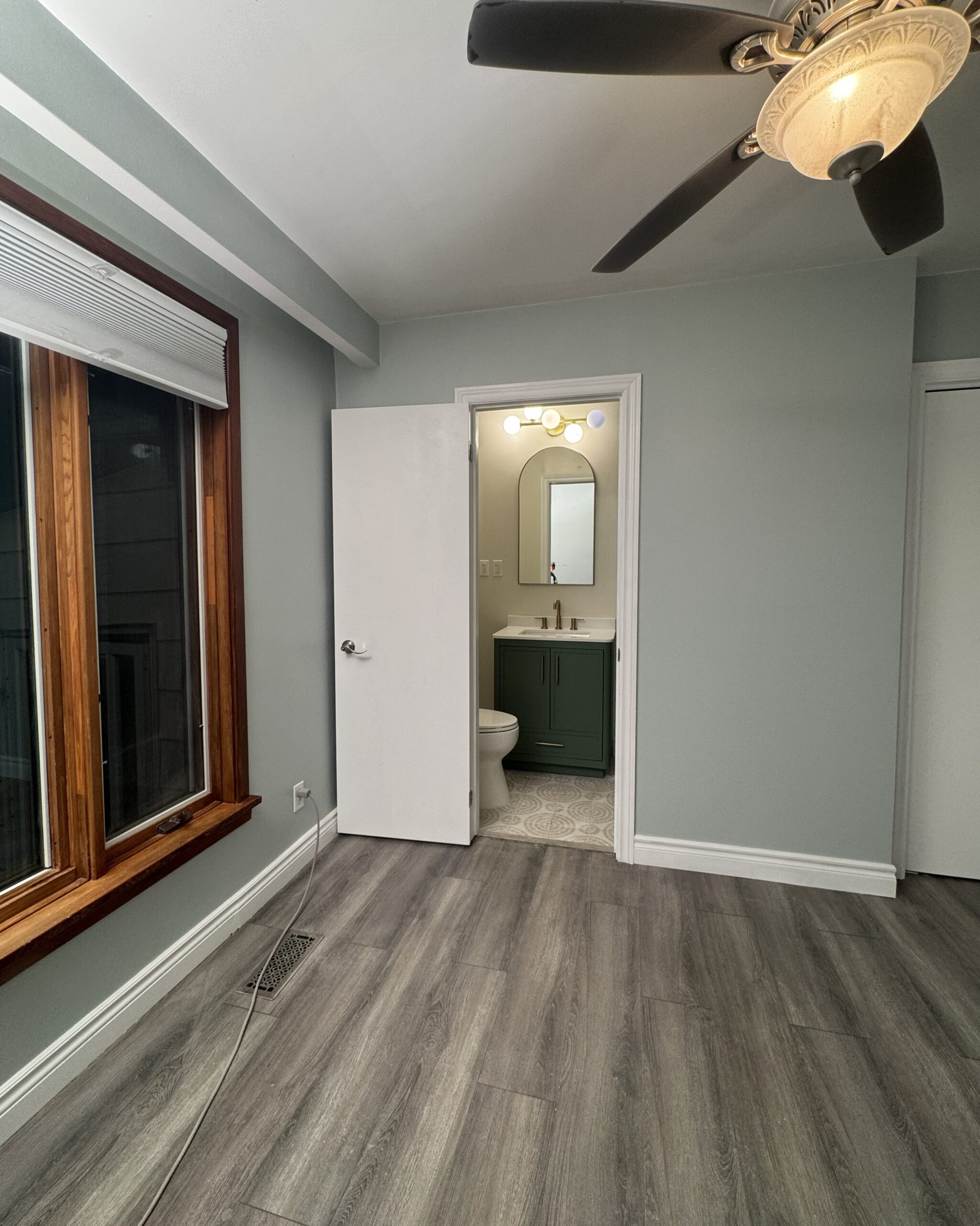 Renovated master bedroom with new grey LVP flooring and open doorway leading to newly added ensuite bathroom in Toronto home