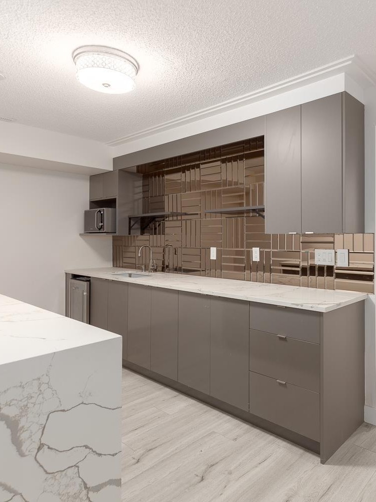 Basement kitchenette with grey flat-panel cabinets, bronze mirrored backsplash, and quartz waterfall countertop in a North York home