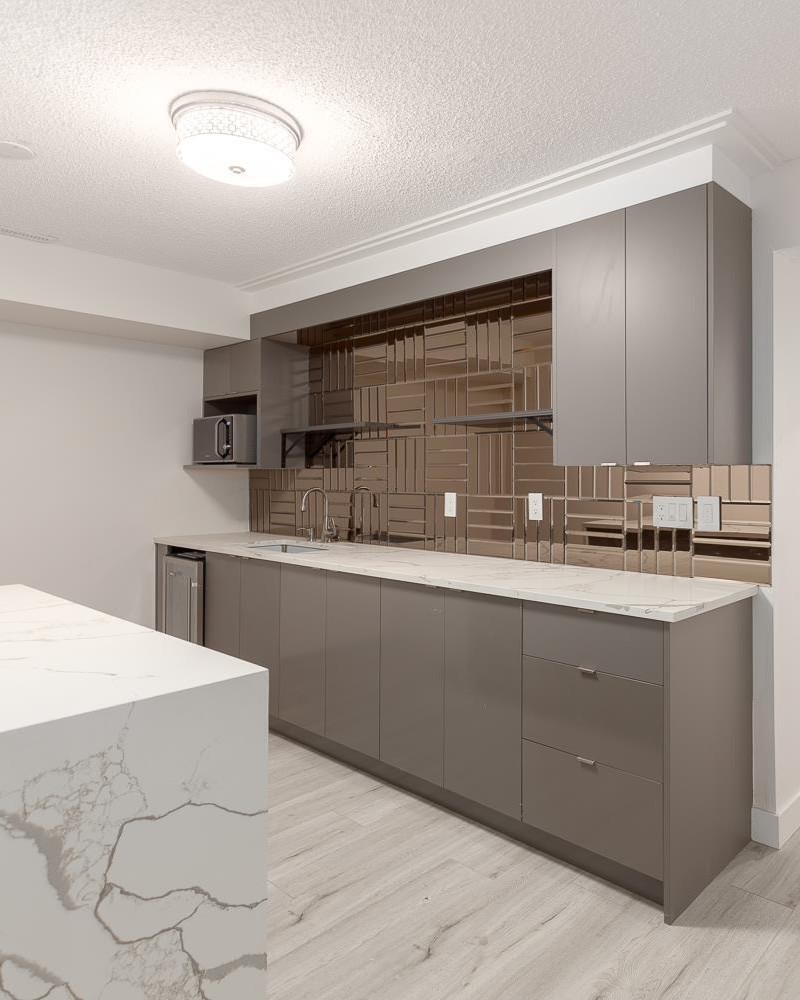 Basement kitchenette with grey flat-panel cabinets, bronze mirrored backsplash, and quartz waterfall countertop in a North York home
