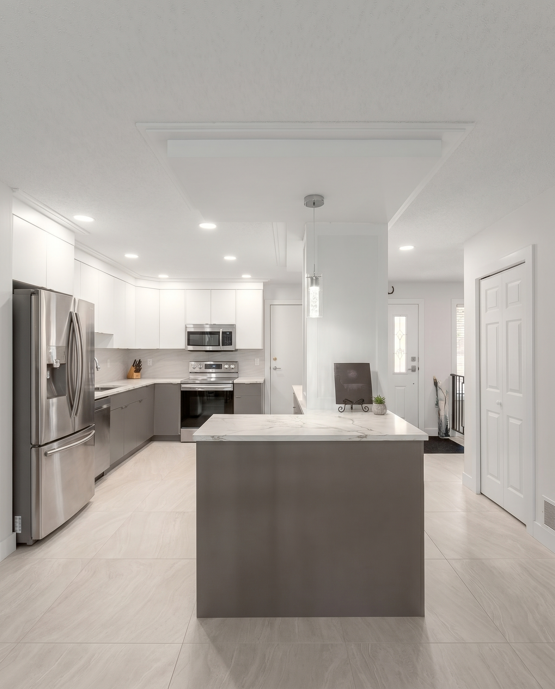 Modern two-tone kitchen with white and grey cabinets, quartz peninsula, and glass pendant lighting in North York